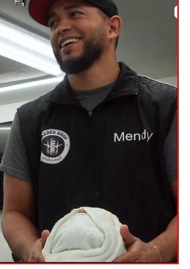 Mendy, owner and lead barber at Unlimited Barbershop in Danbury, CT, smiling in his branded vest and cap